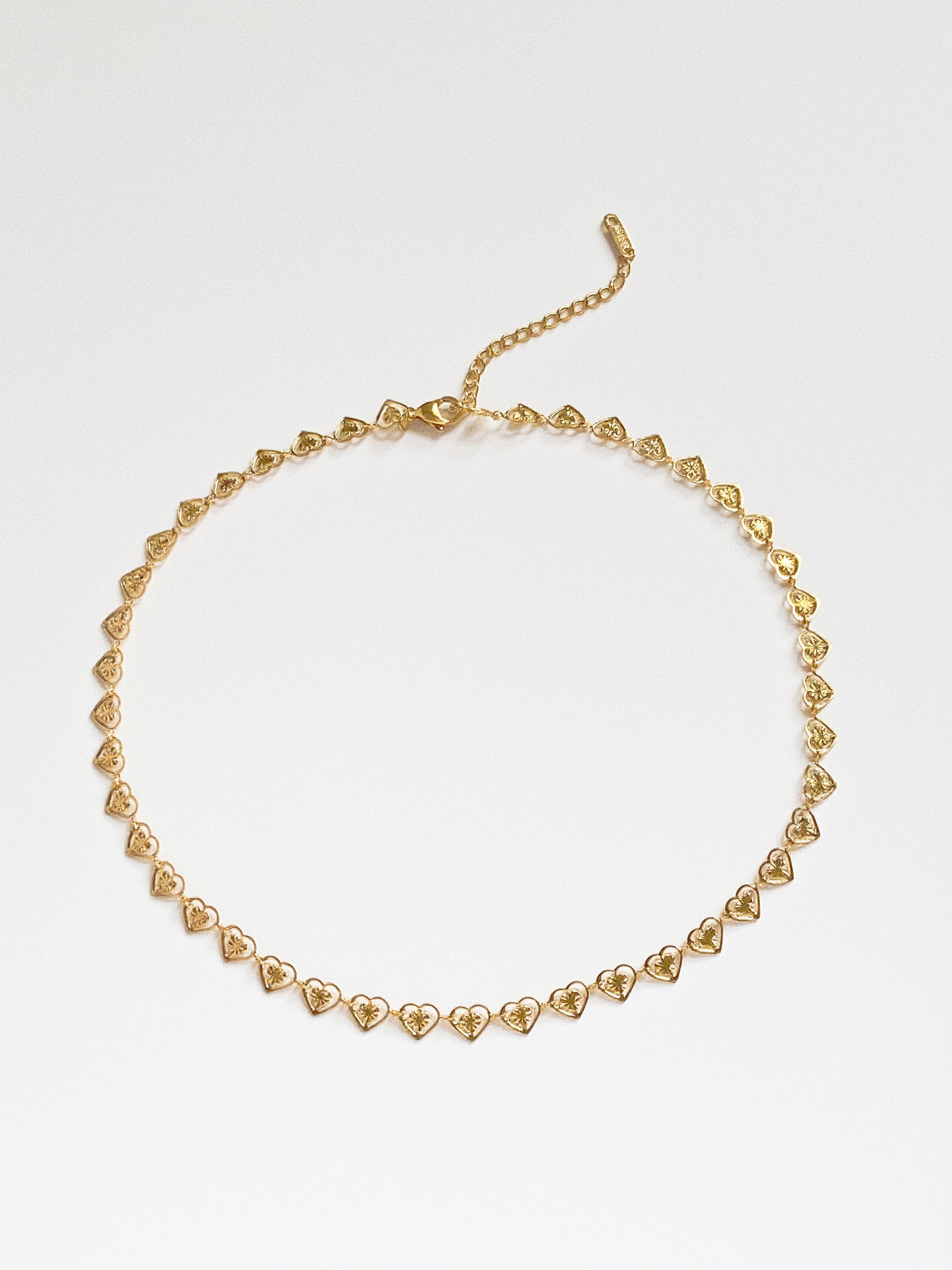 Flat lay view of the gold heart link choker arranged in a circle, showing the continuous reflective diamond-cut texture.