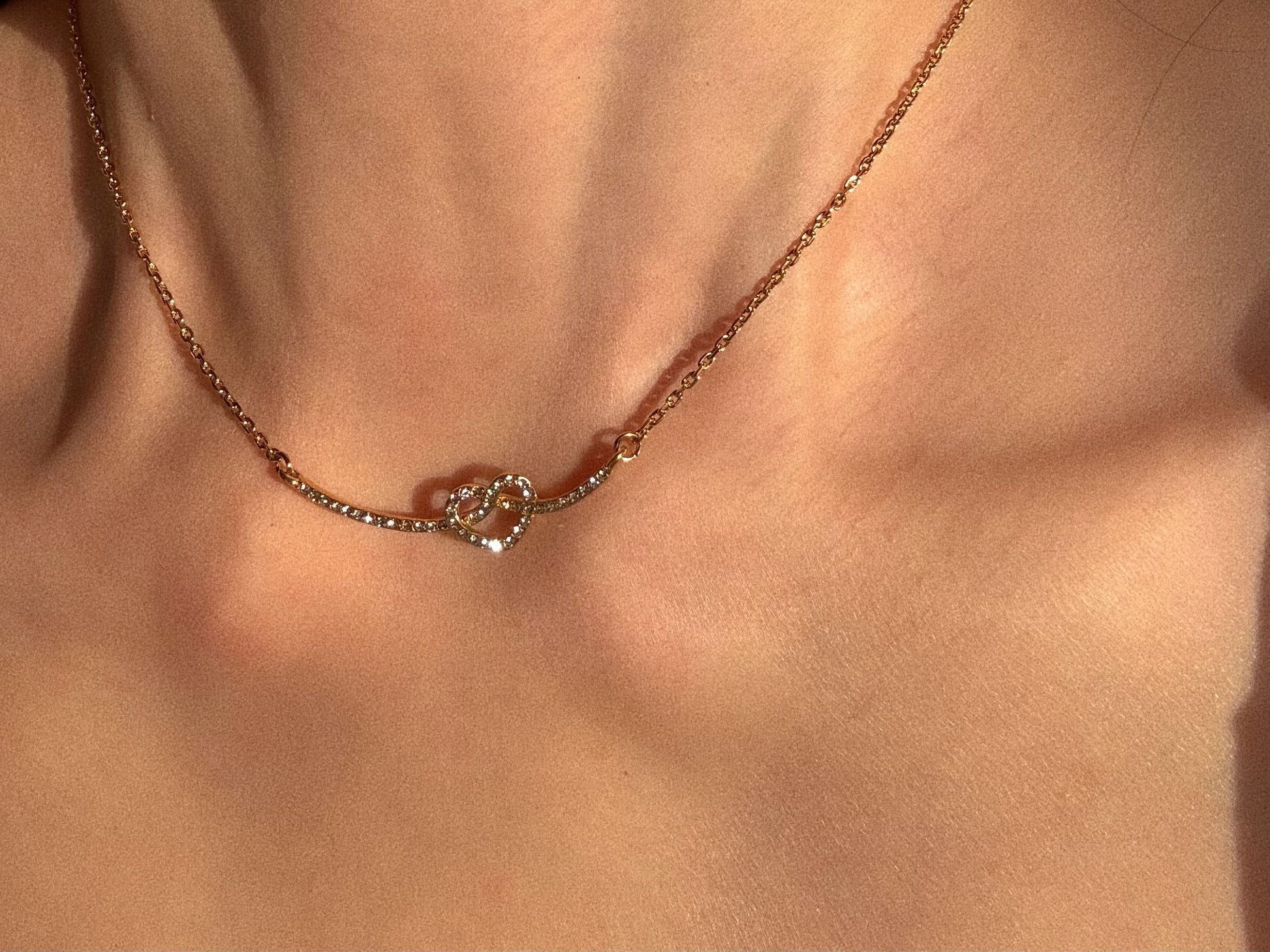 Waterproof gold stainless steel necklace with a knotted heart curved bar design, isolated on white background.