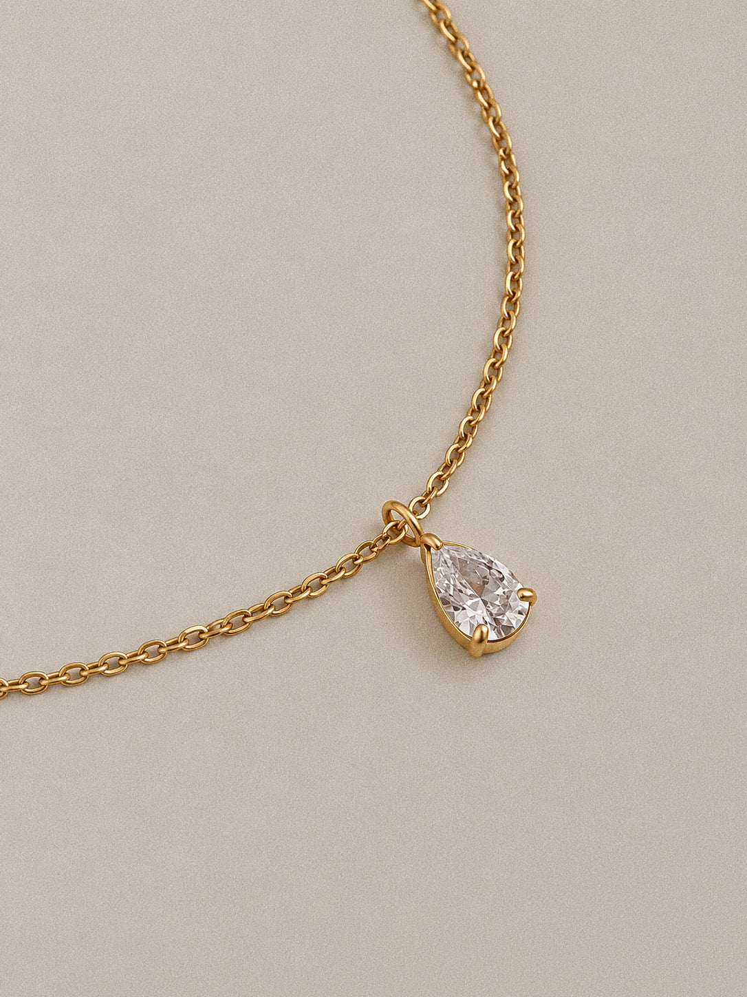Close-up of Goutte's clear pear-shaped stone in a gold-plated claw setting, suspended from a fine link chain.