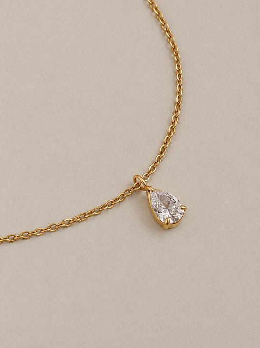 Close-up of Goutte's clear pear-shaped stone in a gold-plated claw setting, suspended from a fine link chain.