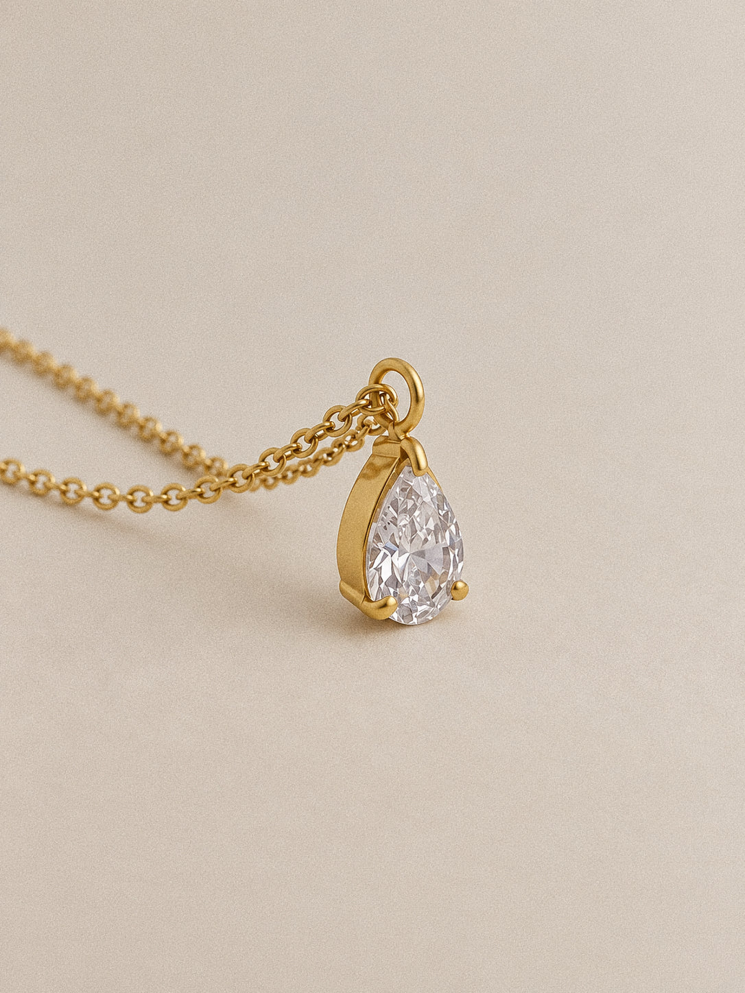 Angled view of the Goutte pendant, showing the faceted pear-shaped stone, three claws and gold-plated setting.