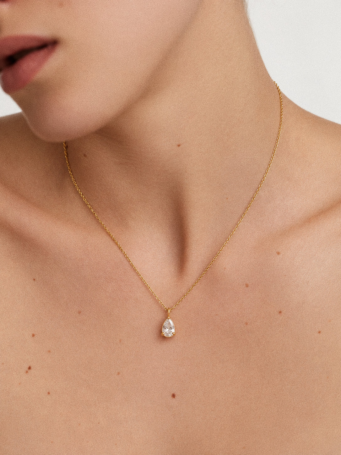 Goutte teardrop pendant necklace worn alone on a model, with the clear stone hanging from a fine gold-plated chain.