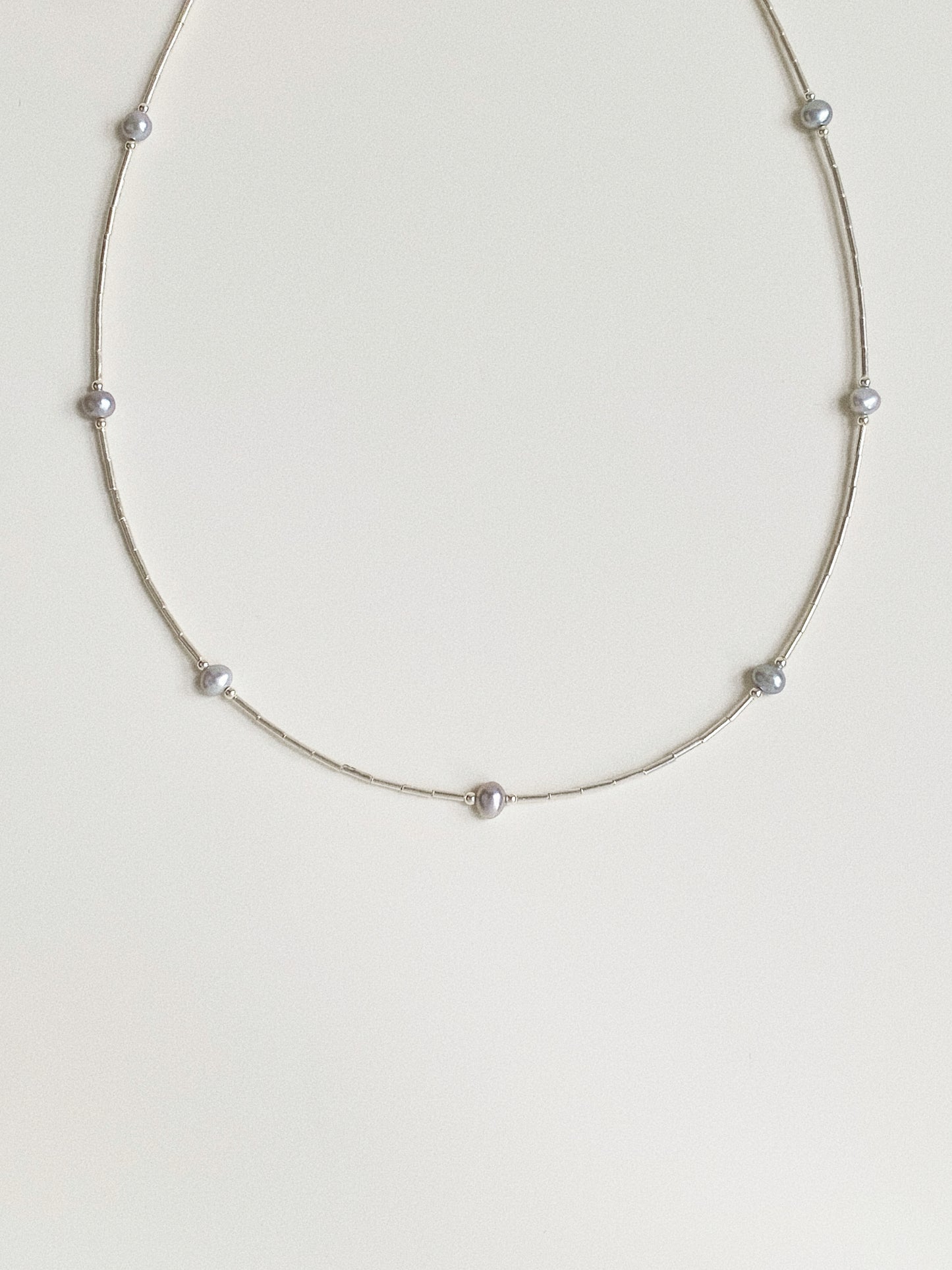Full view of dainty grey pearl station necklace on 925 sterling silver chain laid flat