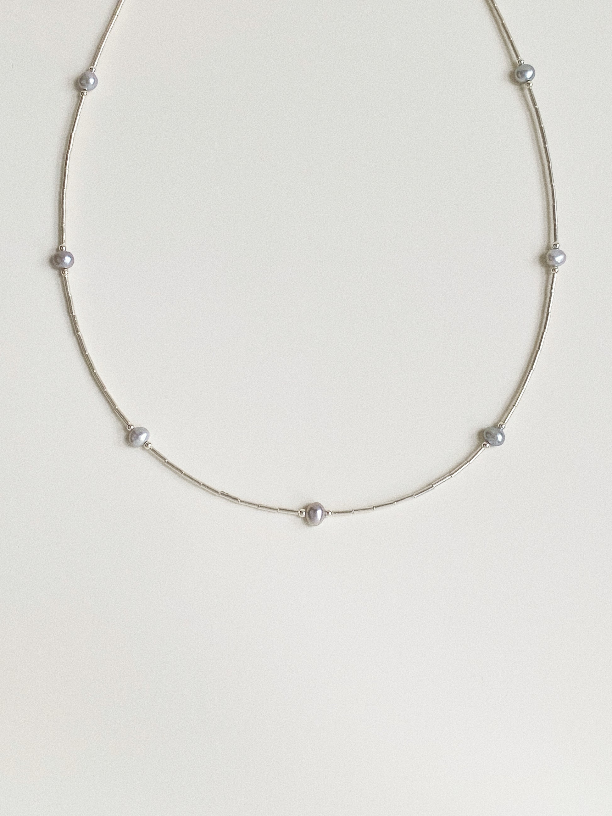 Full view of dainty grey pearl station necklace on 925 sterling silver chain laid flat