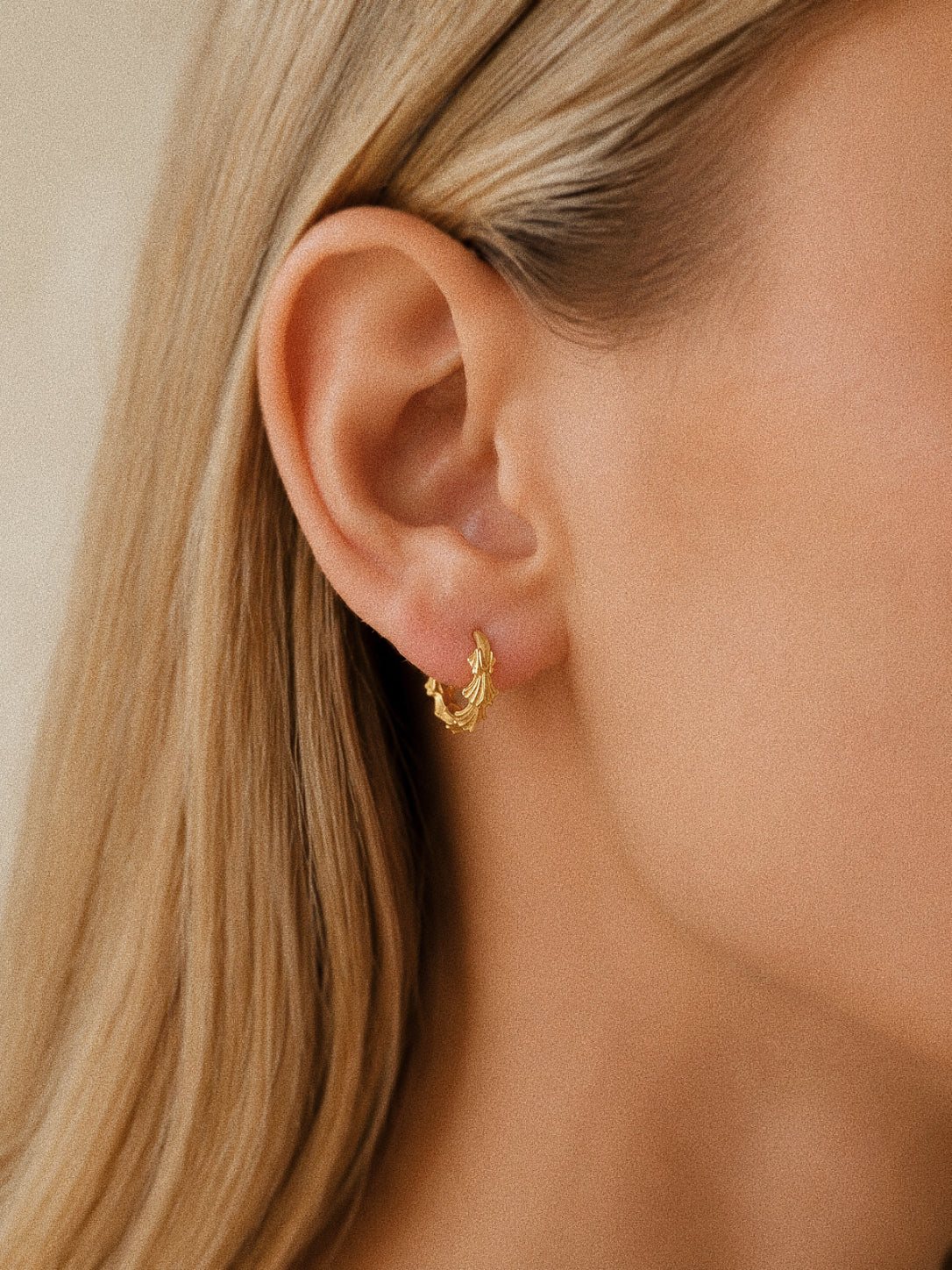 Grove gold leaf huggie hoop earrings worn on the ear, showing the 10 mm scale and sculpted leaf detail.