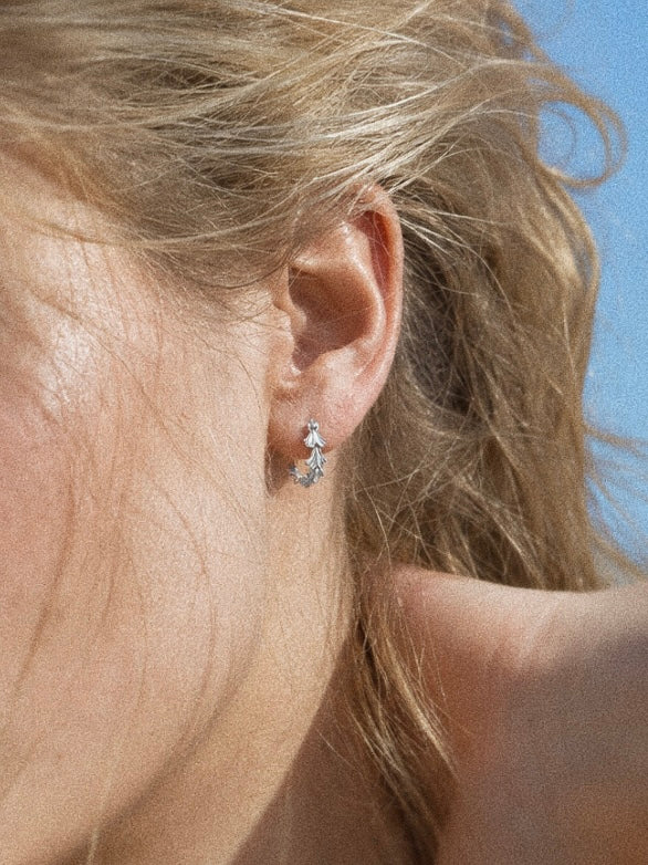 Grove sterling silver leaf hoop earrings worn on the ear, showing their small close-fitting botanical design.