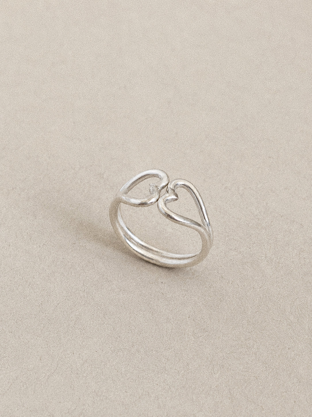 Angled view of a handmade double heart ring in 925 sterling silver, two open hearts meeting point to point on a twin band.