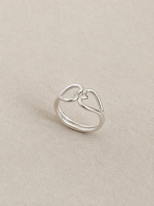 Angled view of a handmade double heart ring in 925 sterling silver, two open hearts meeting point to point on a twin band.