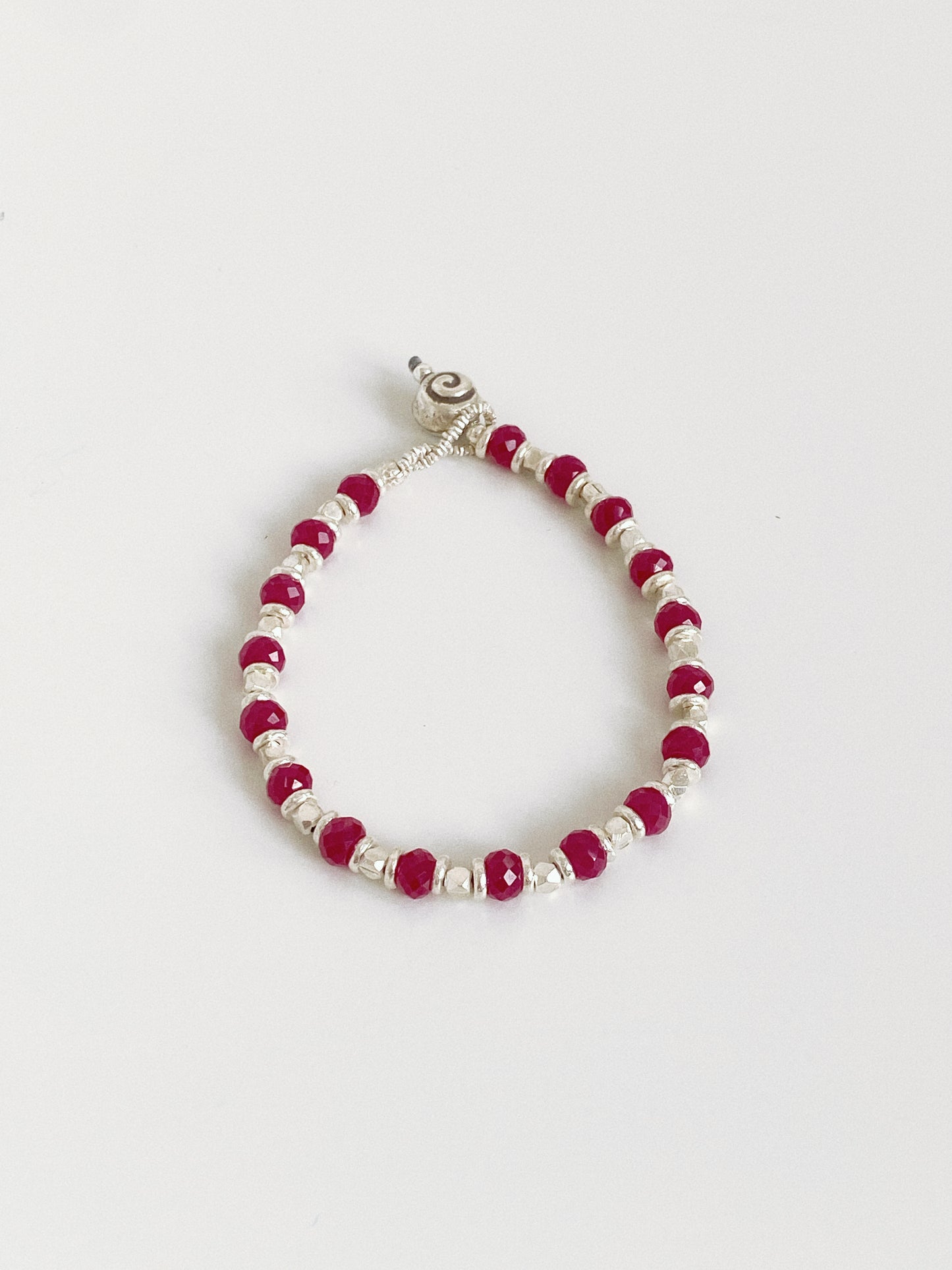 Handmade red corundum and silver bead bracelet lying flat, hand strung facets catching the light.