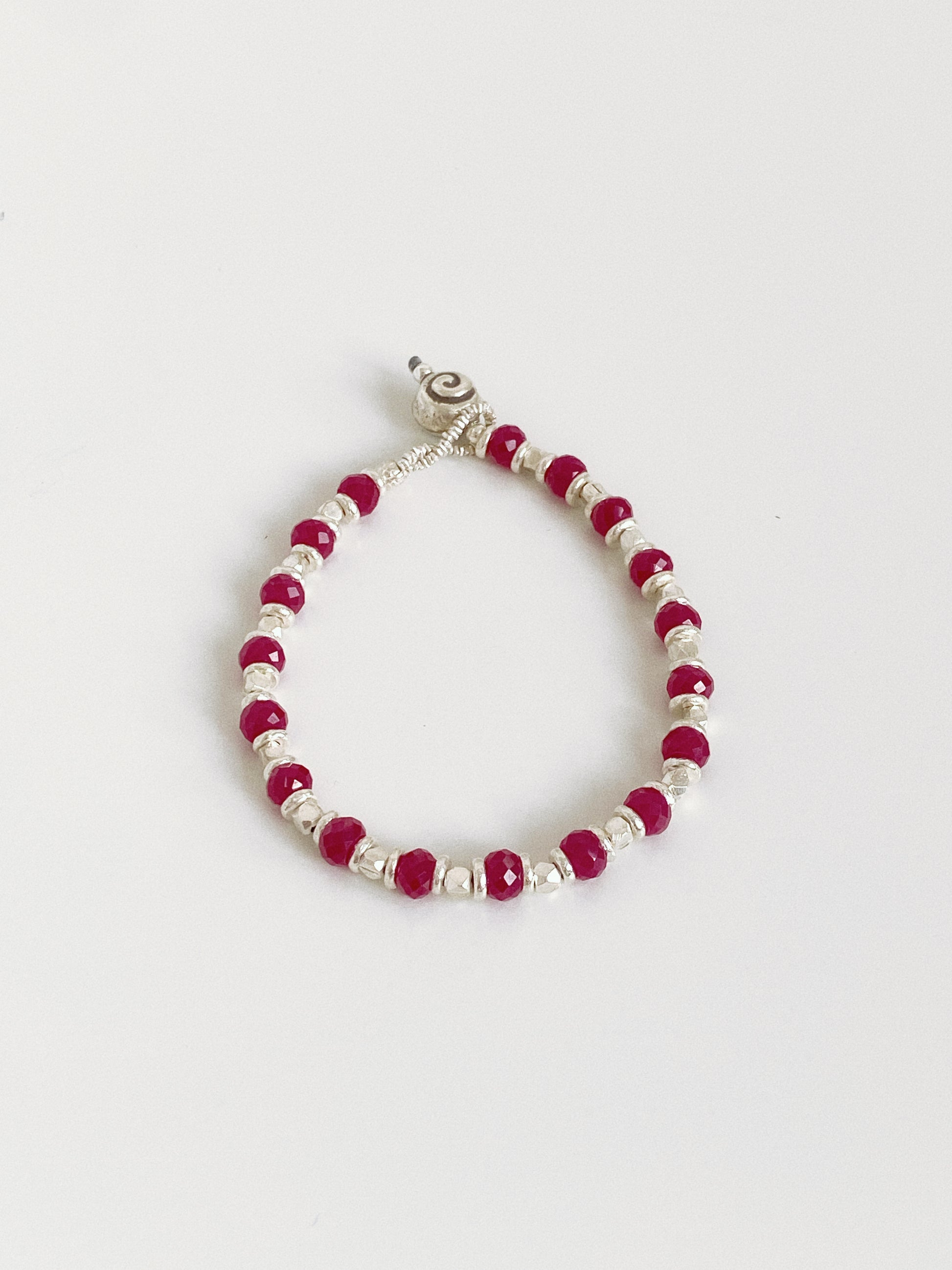 Handmade red corundum and silver bead bracelet lying flat, hand strung facets catching the light.