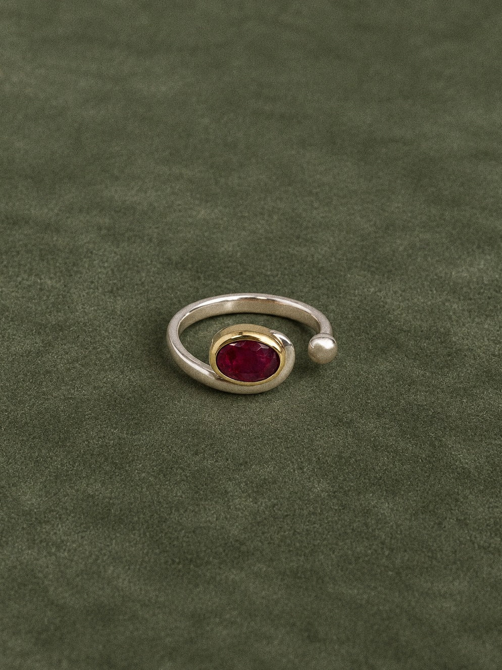 Handmade sterling silver and brass ruby ring standing upright on an olive velvet background