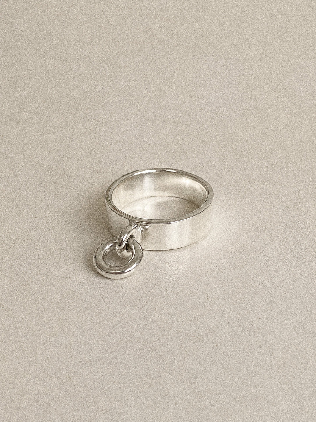 Angled view of a handmade silver charm ring, a wide polished 925 band with a small hoop hanging at its edge.