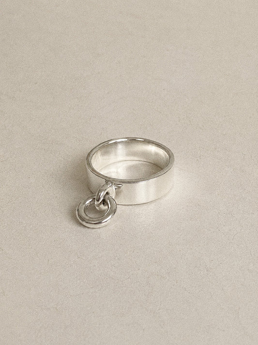 Angled view of a handmade silver charm ring, a wide polished 925 band with a small hoop hanging at its edge.
