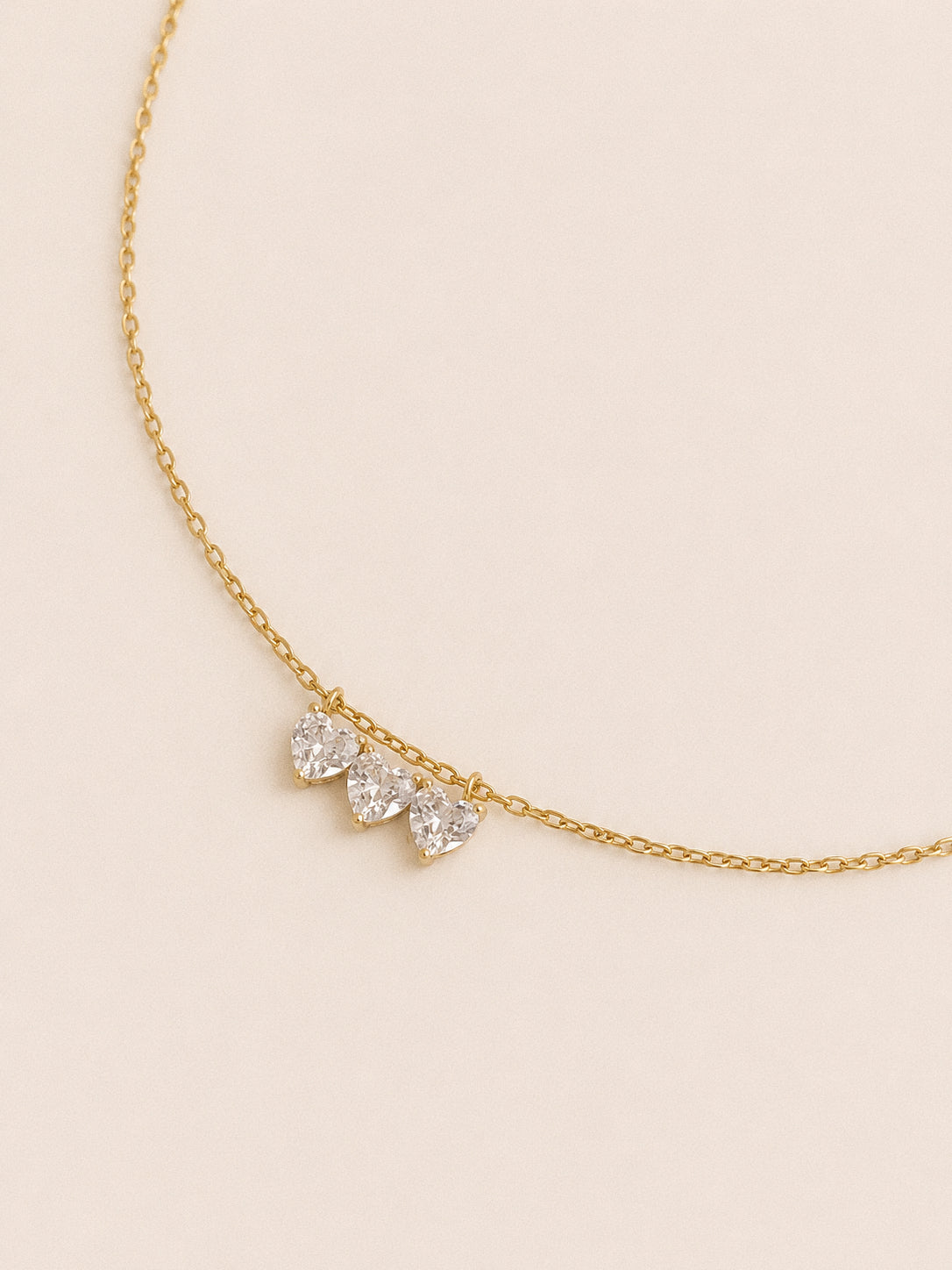 Side angle of the three heart cut cz stones sitting flat along the gold chain of the Trio necklace
