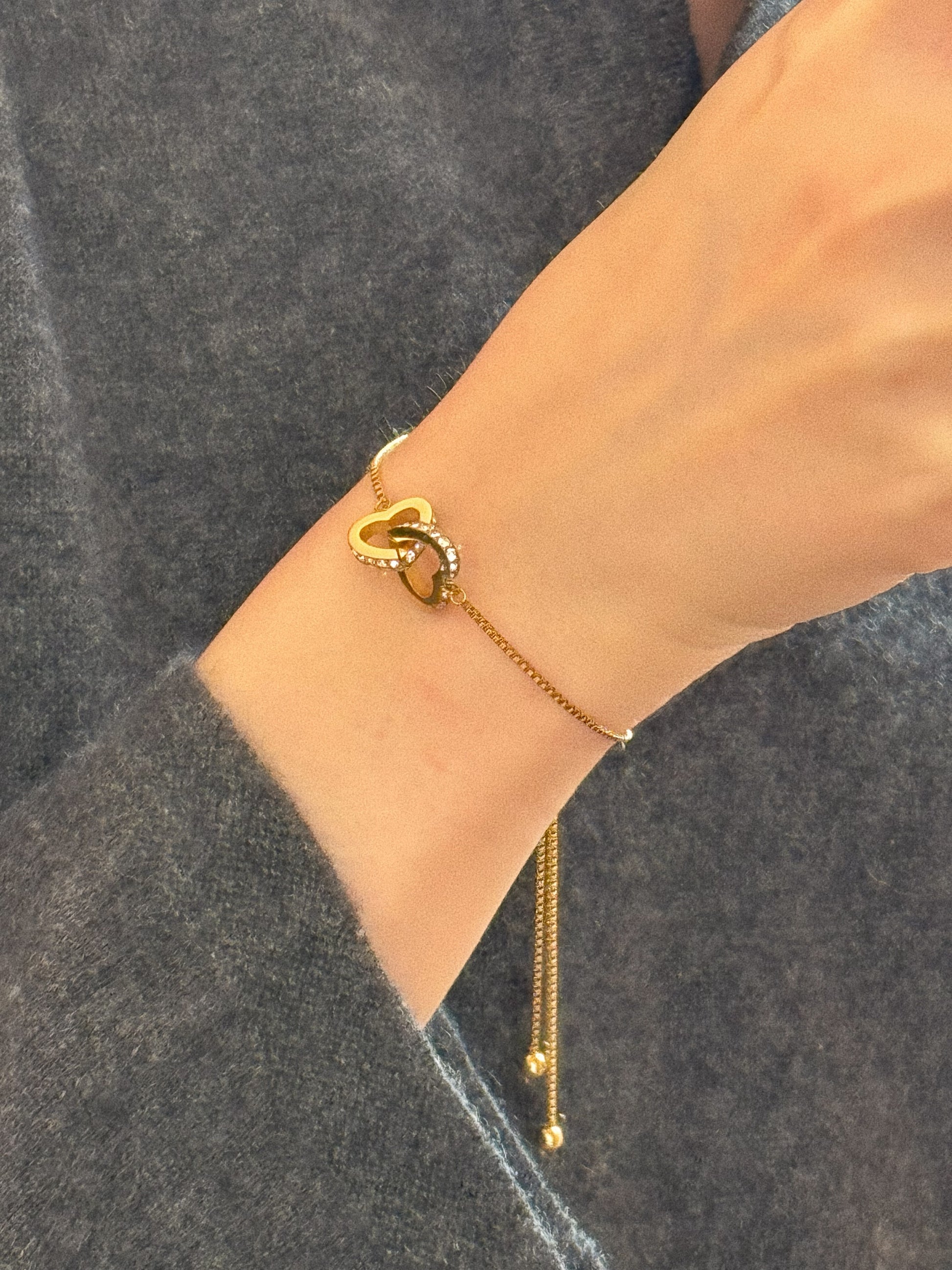 Woman wearing gold interlocking hearts bracelet on wrist, featuring pave crystals and adjustable chain.