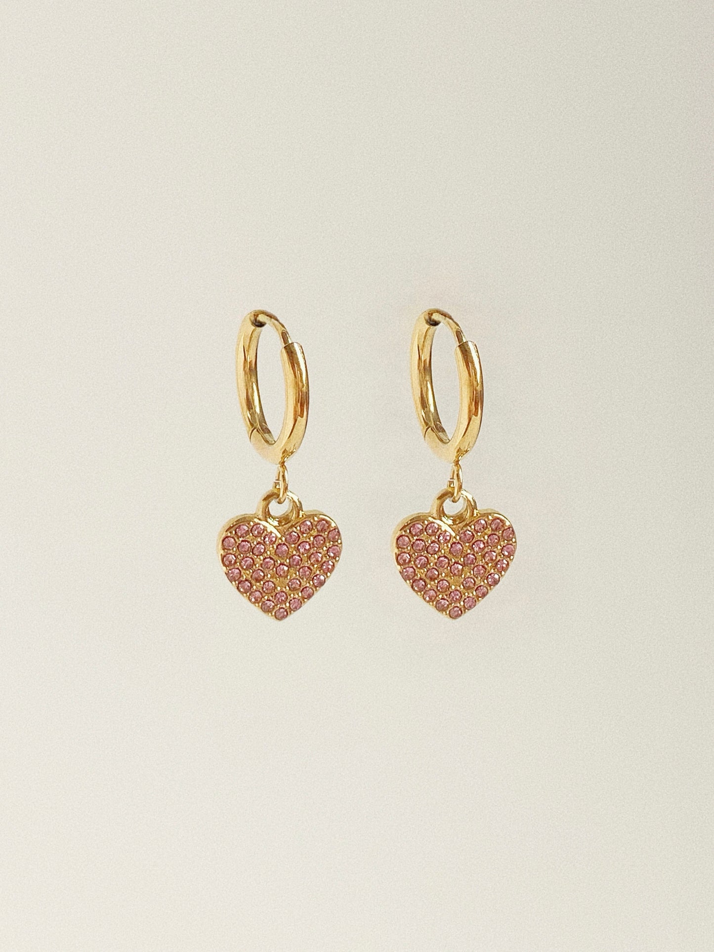 Isolated pair of gold hoop earrings featuring pink pave cubic zirconia heart charms.