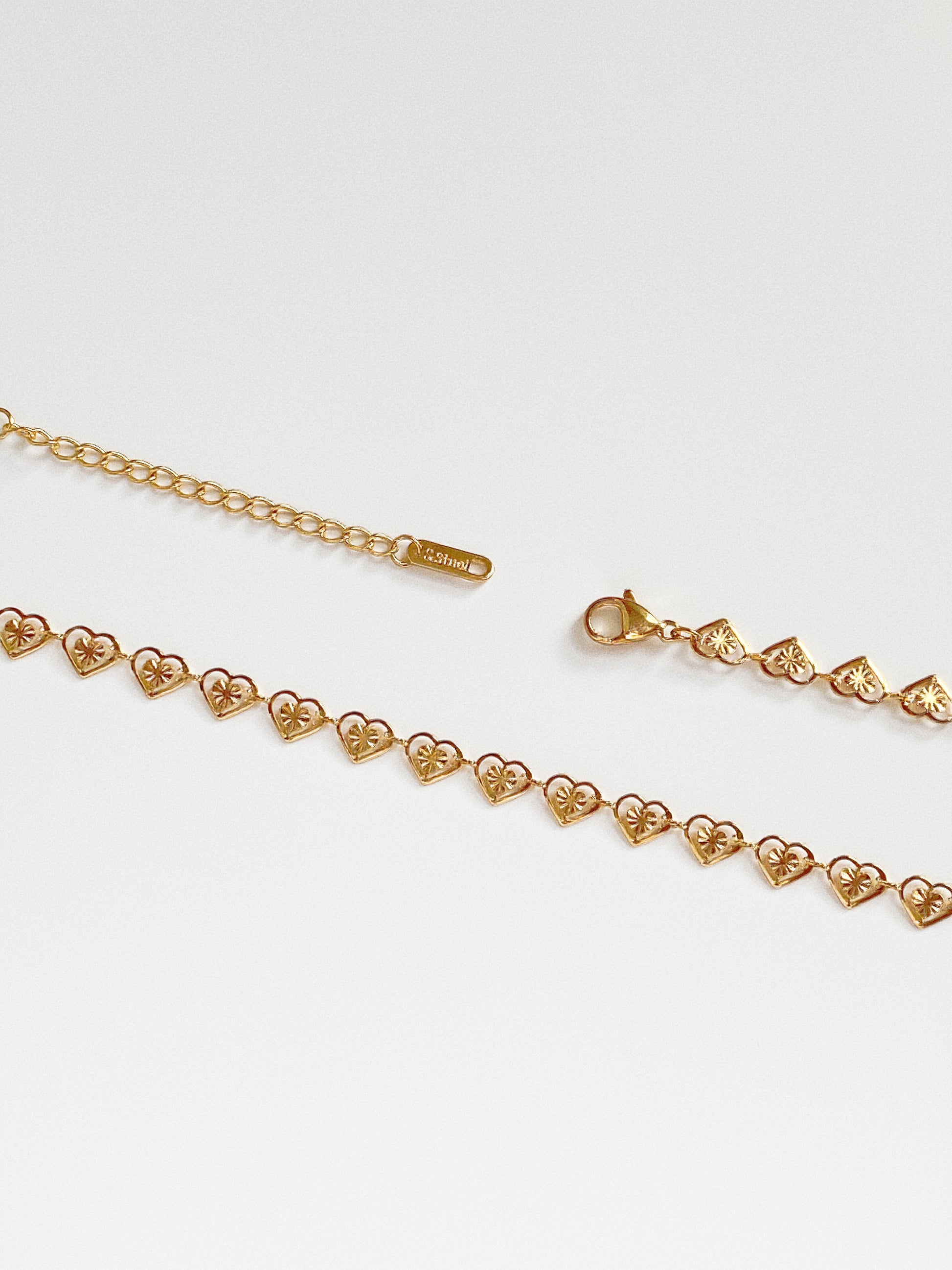 Close up detail of the gold heart chain showing the stainless steel stamp on the extender tag, verifying waterproof quality.