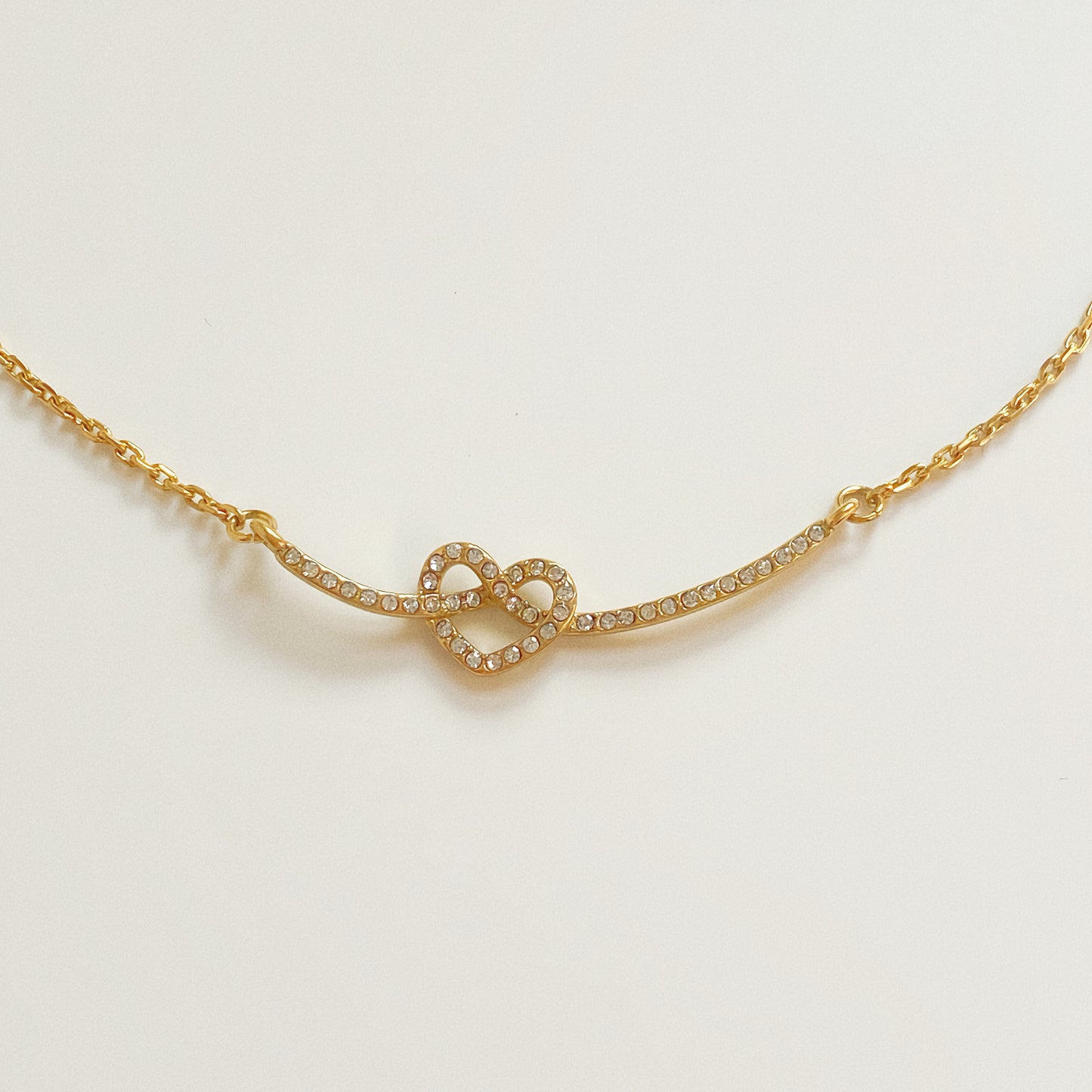 Gold love knot smile necklace isolated on white background, featuring a twisted rope bar and interlocking heart pendant.