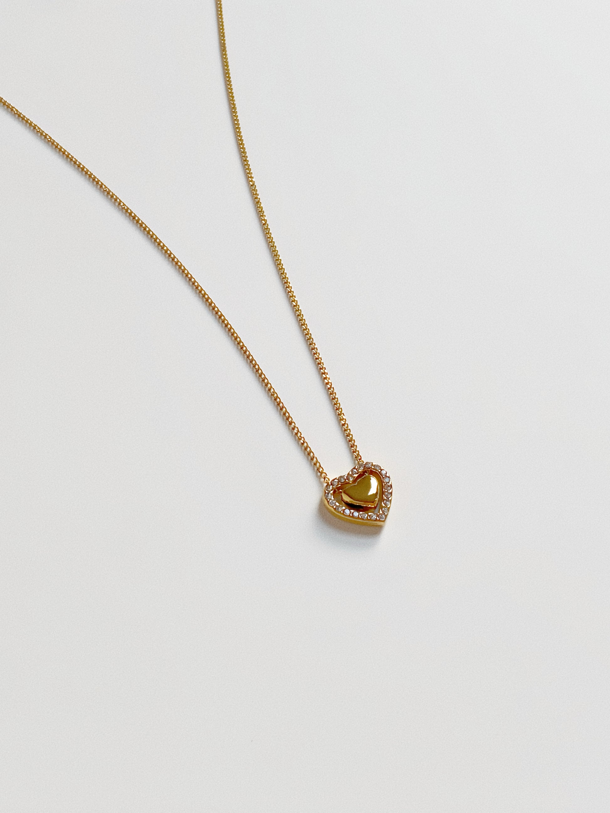 Close up of the dancing heart pendant, featuring a solid gold heart suspended inside a crystal-lined heart frame.
