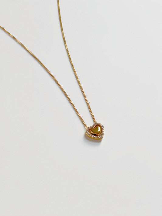 Close up of the dancing heart pendant, featuring a solid gold heart suspended inside a crystal-lined heart frame.