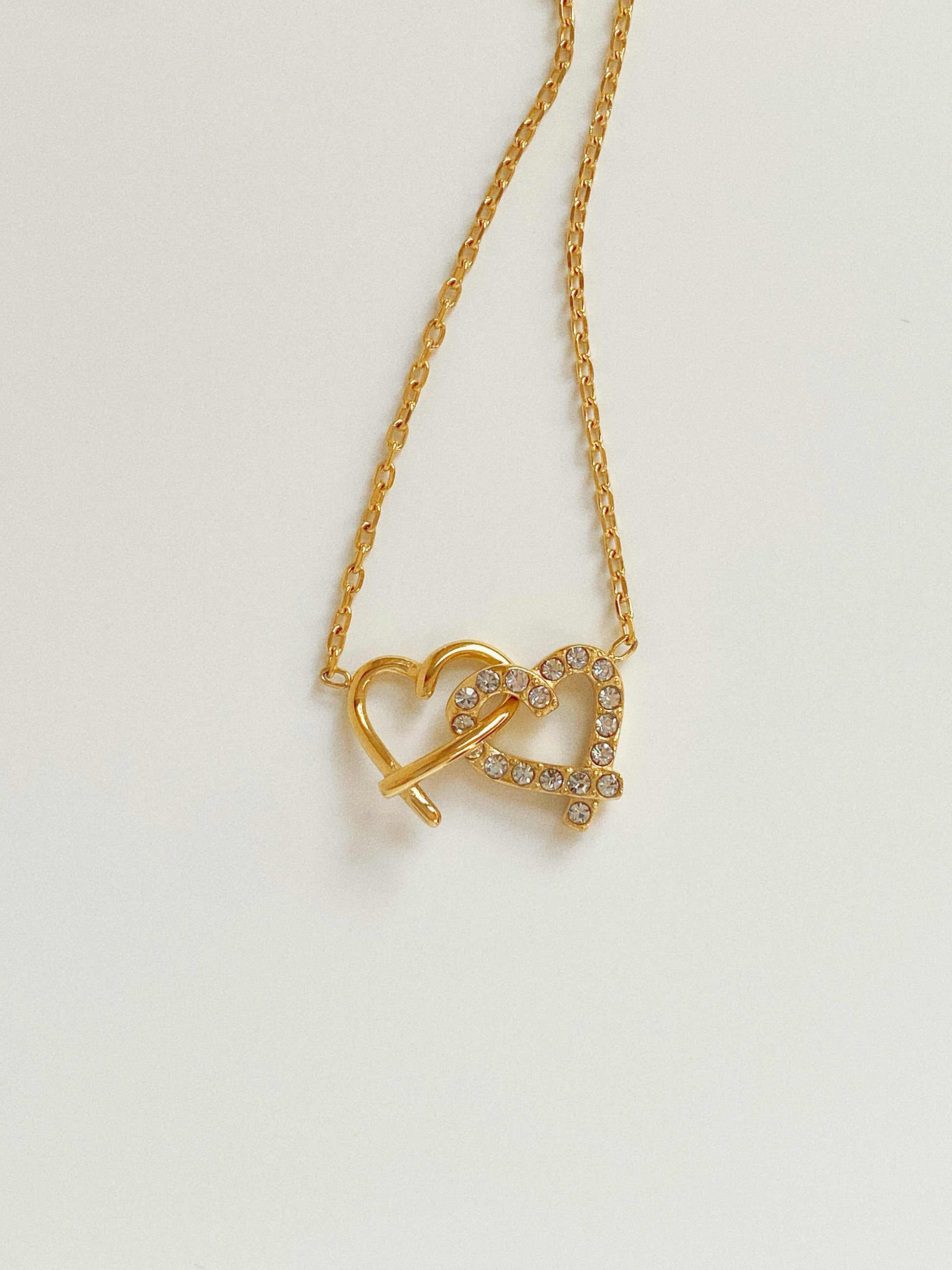 Close up of interlocking heart pendant featuring one polished gold heart and one pave crystal heart.