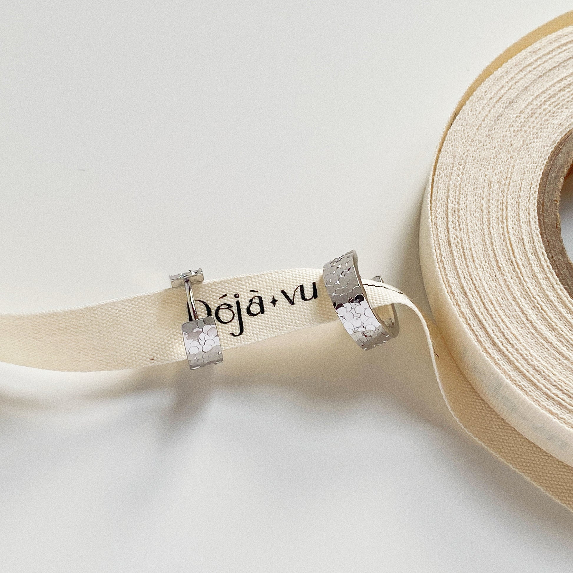 Dainty silver textured hoops styled on a cream ribbon, focusing on the facet details.