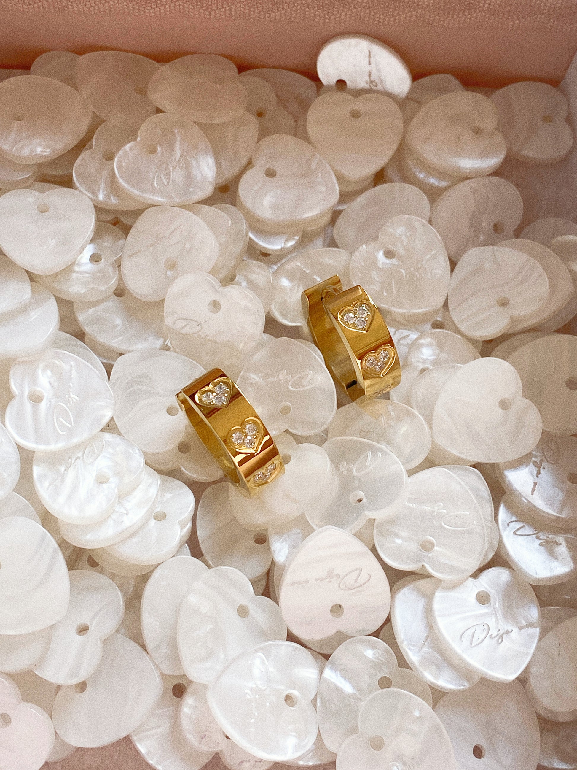 Chunky gold wide hoop earrings with etched crystal hearts, displayed in a box with mother-of-pearl shells.