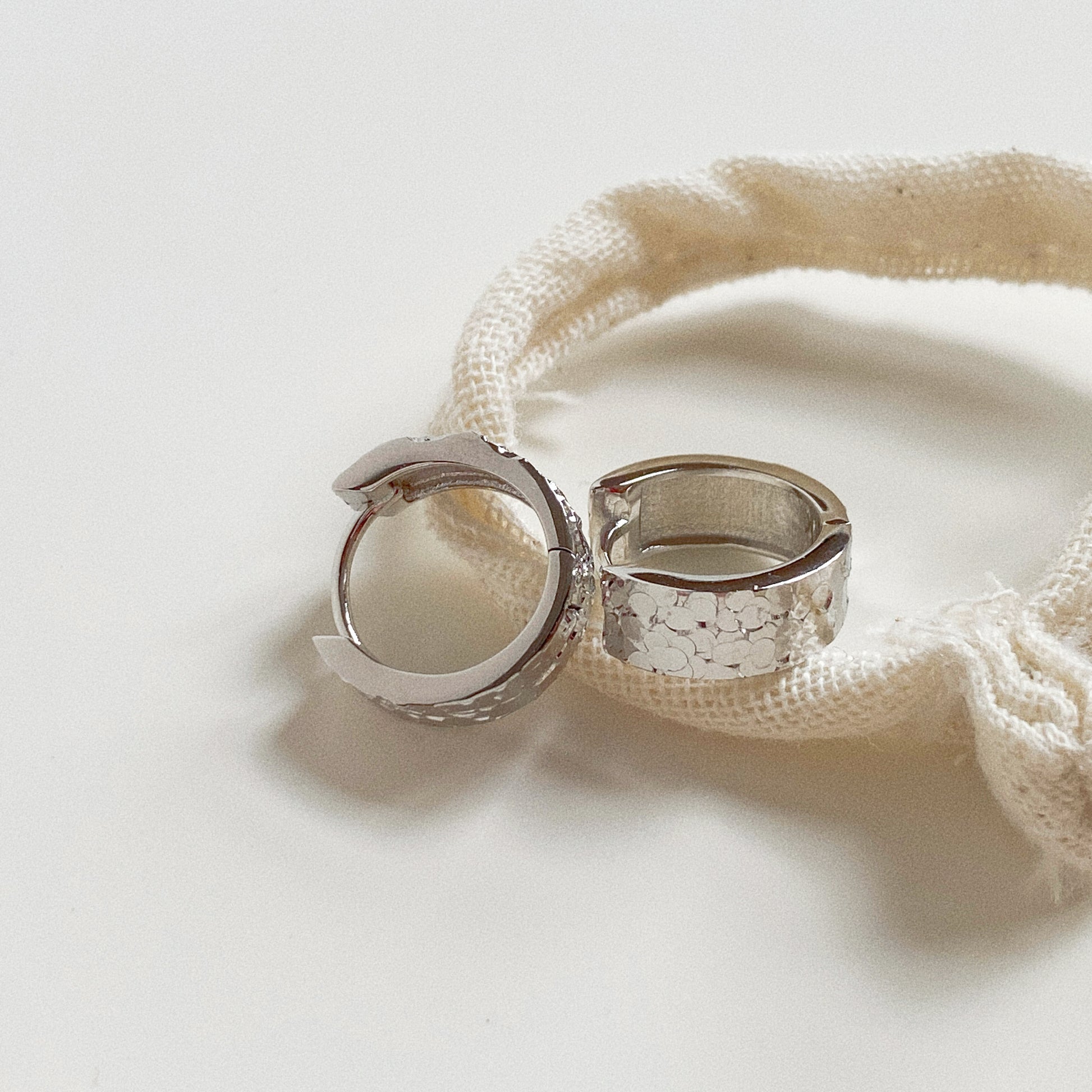 Pair of 925 Sterling Silver textured huggie earrings displayed on a Deja Vu canvas pouch.