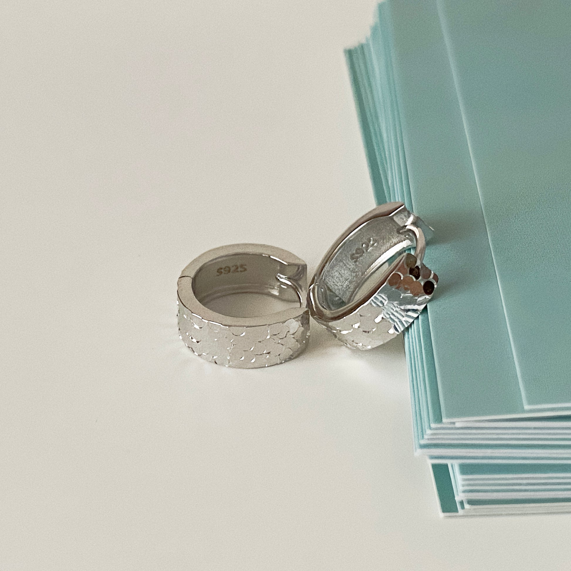 Silver sleeper earrings with diamond-cut texture, resting next to green stationery.