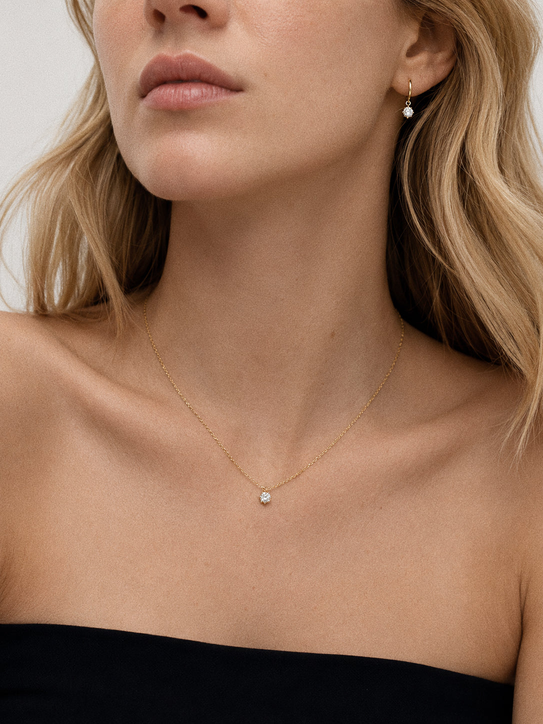 Model wearing the Icon solitaire necklace with the matching Icon huggie earrings in 18k gold