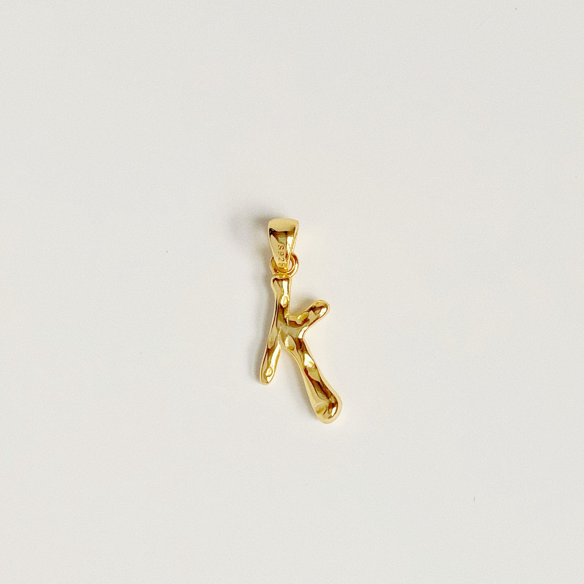 Close up of 18k Gold Vermeil molten texture letter K pendant charm isolated on white background.
