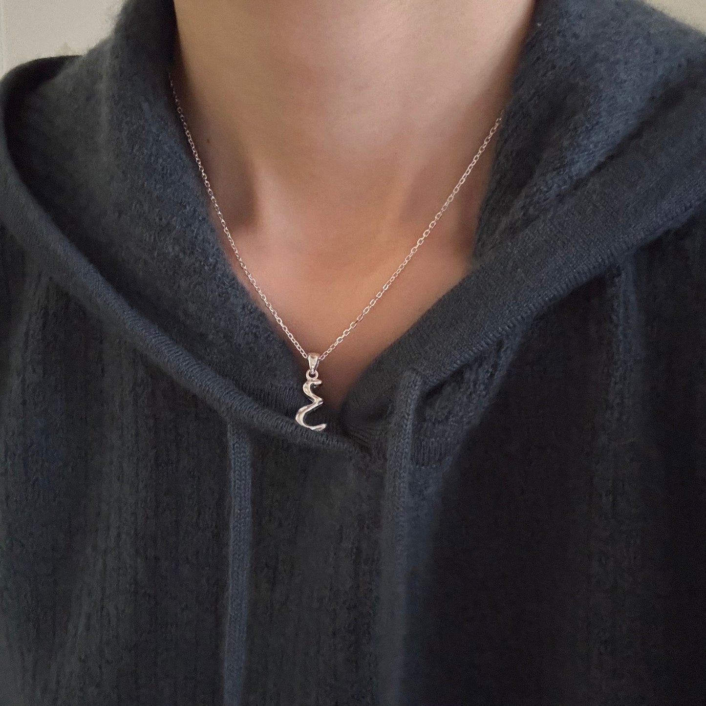 Model wearing silver molten initial necklace styled with a casual grey hoodie to show length and fit.