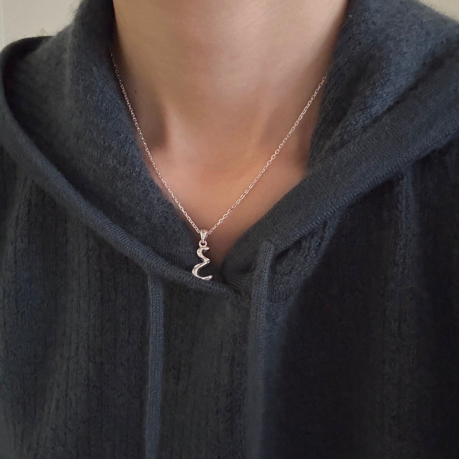 Model wearing silver molten initial necklace styled with a casual grey hoodie to show length and fit.