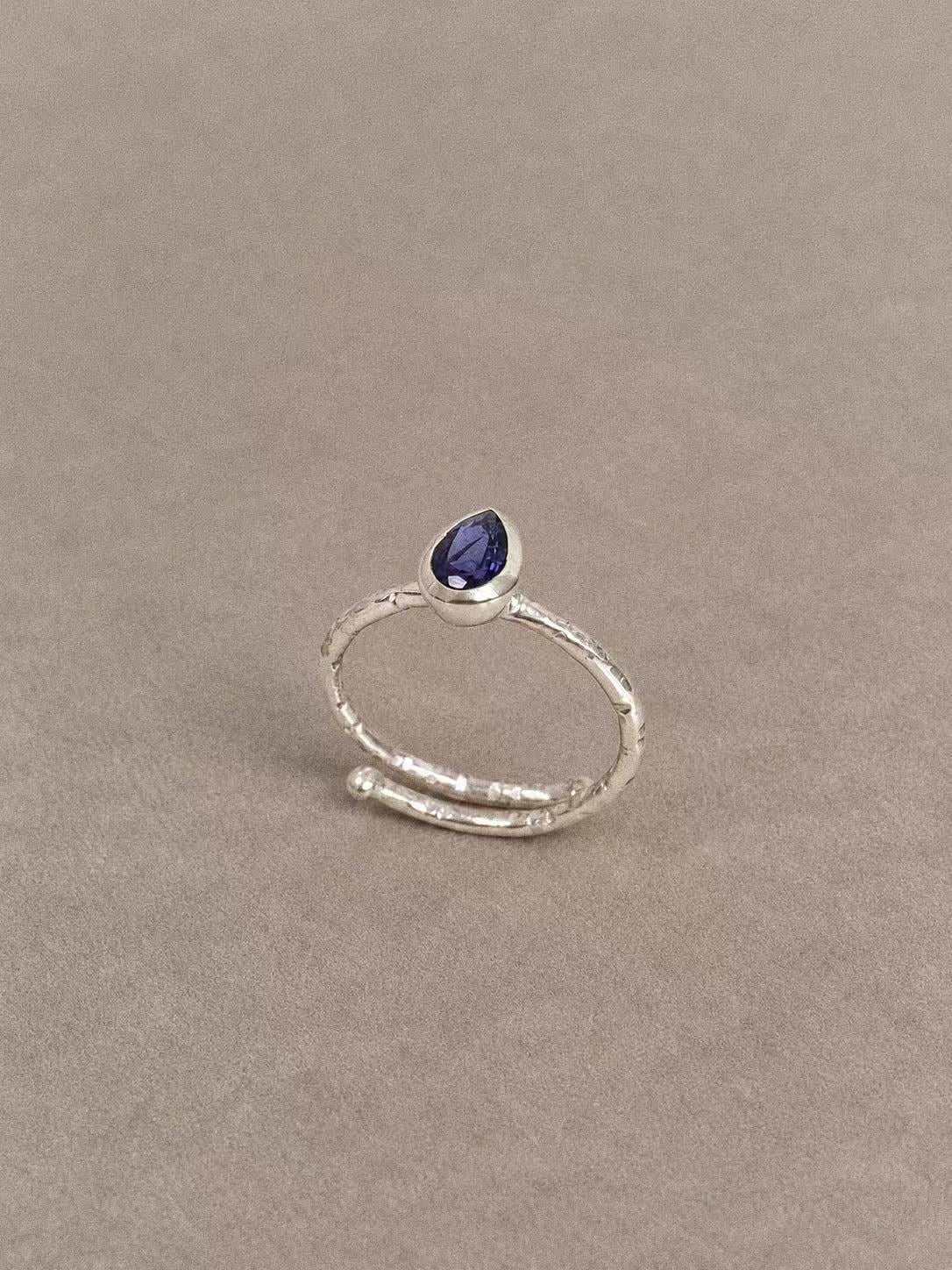 Angled view of the iolite teardrop ring showing its violet-blue faceted gemstone and textured silver band