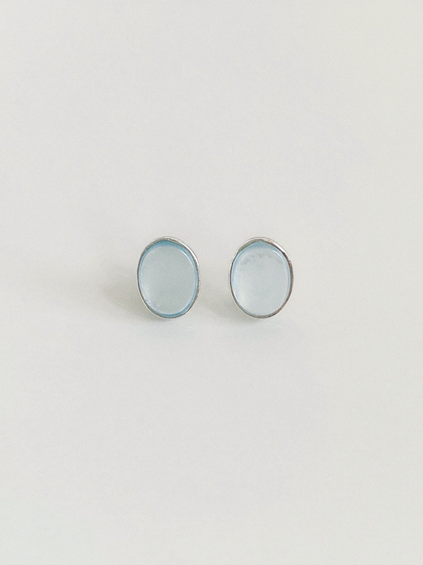 Pair of natural aquamarine oval cabochon stud earrings in textured sterling silver bezels on a warm white background