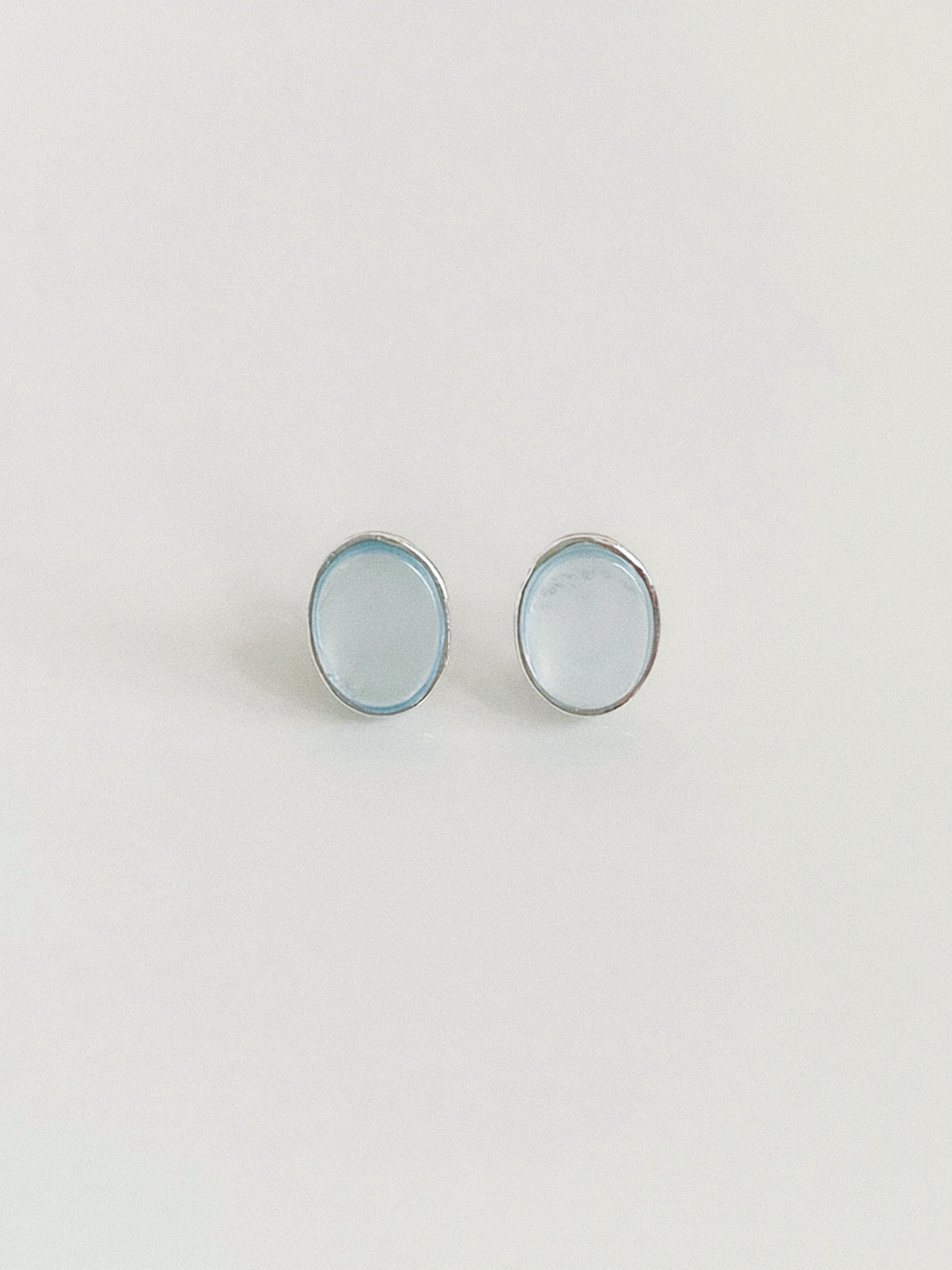 Pair of natural aquamarine oval cabochon stud earrings in textured sterling silver bezels on a warm white background