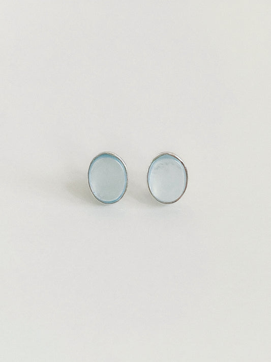 Pair of natural aquamarine oval cabochon stud earrings in textured sterling silver bezels on a warm white background