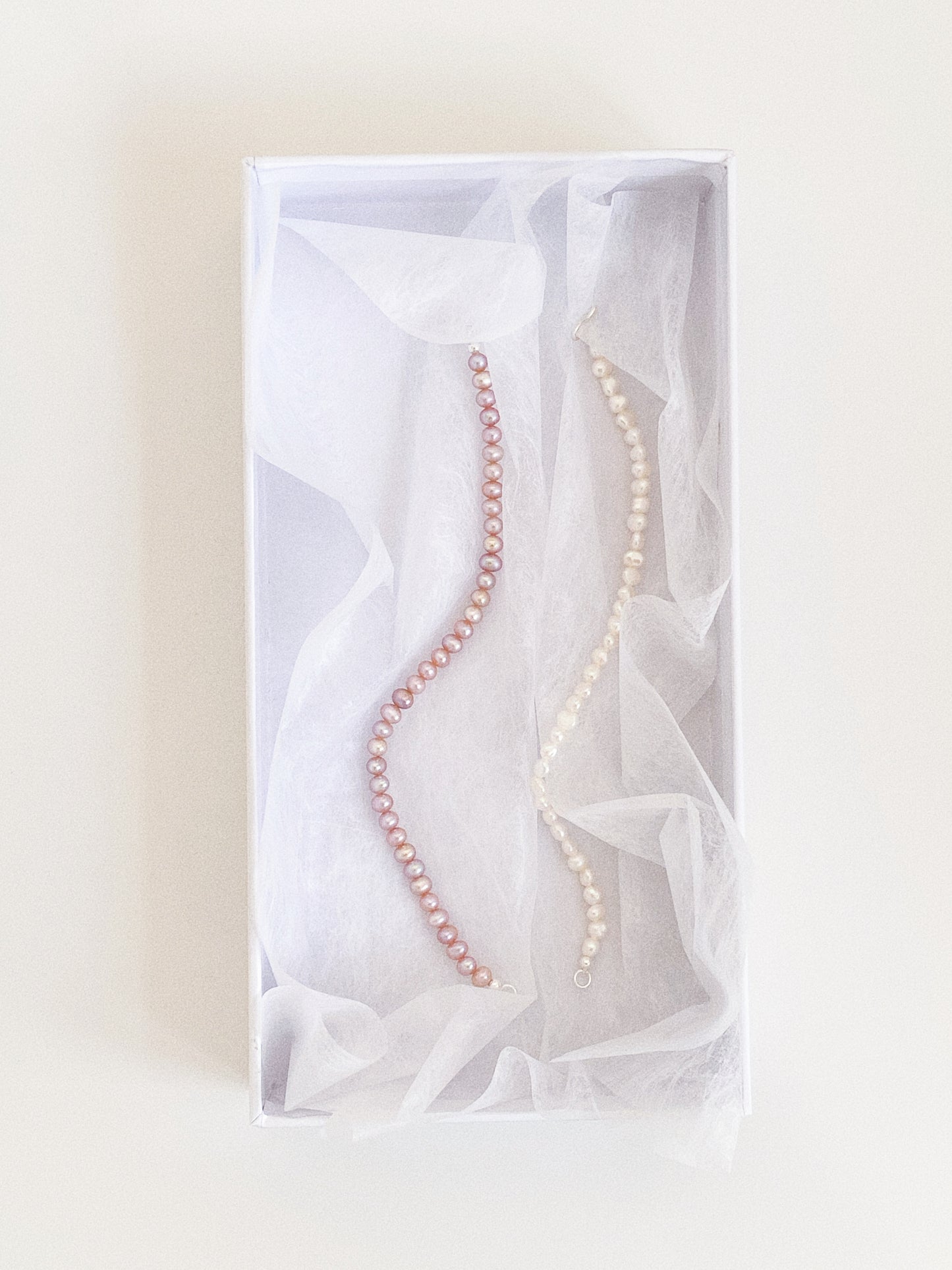 Lavender pink and white freshwater pearl bracelets nestled in soft tissue inside a white gift box