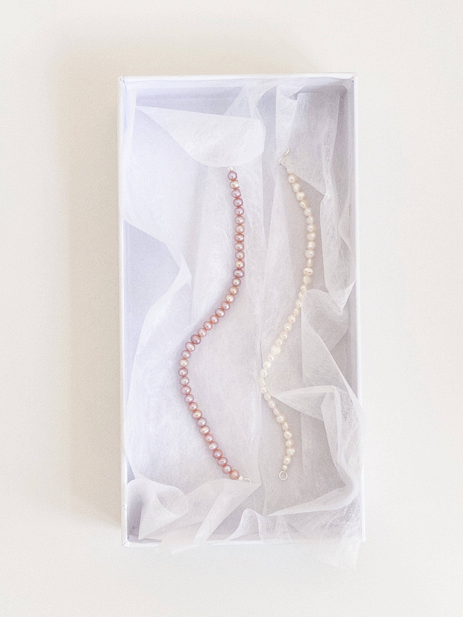 Lavender pink and white freshwater pearl bracelets nestled in soft tissue inside a white gift box