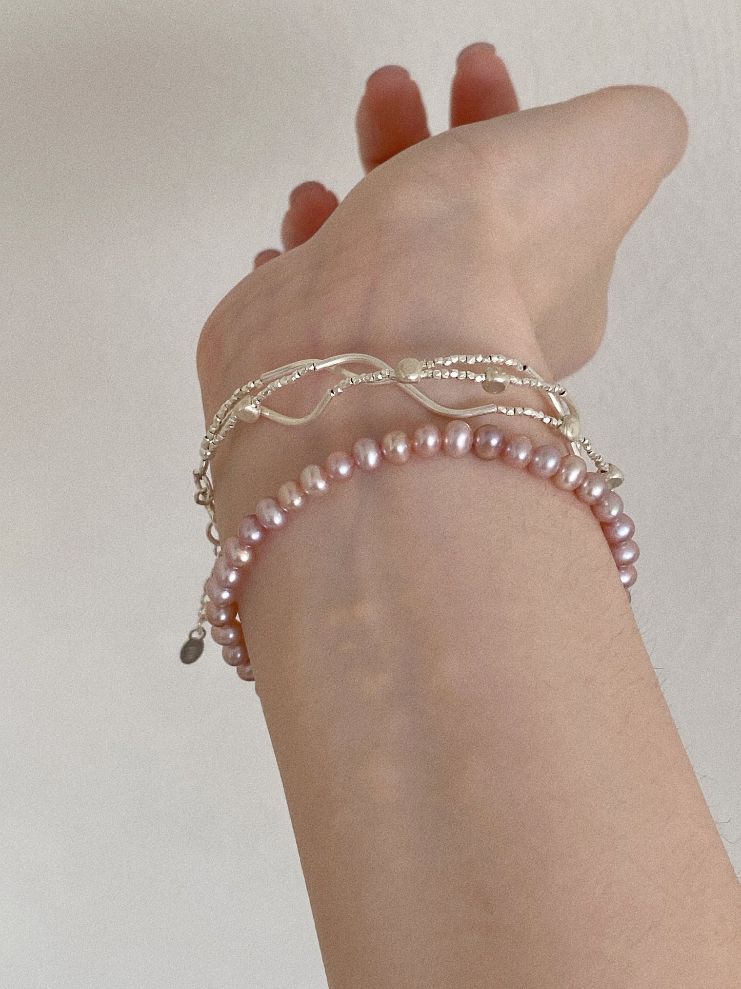 Lavender pink freshwater pearl bracelet worn on the wrist stacked with delicate sterling silver bracelets