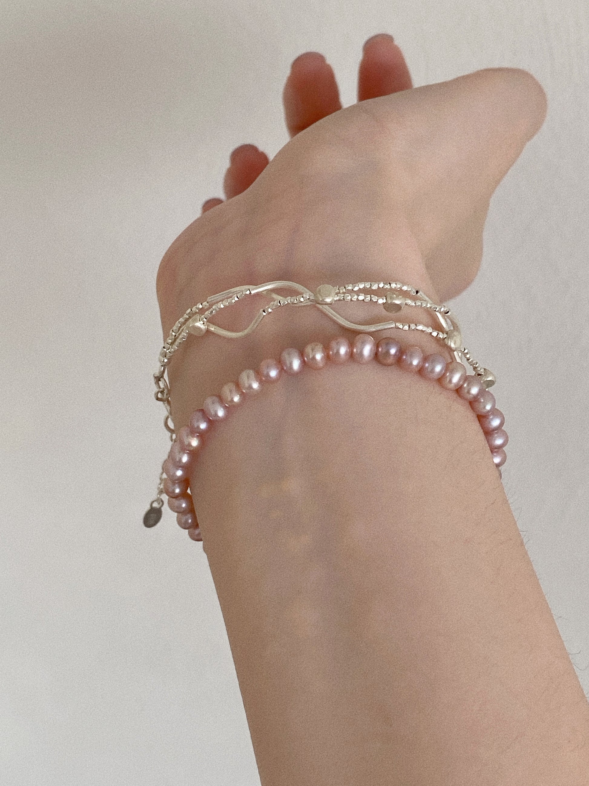Lavender pink freshwater pearl bracelet worn on the wrist stacked with delicate sterling silver bracelets