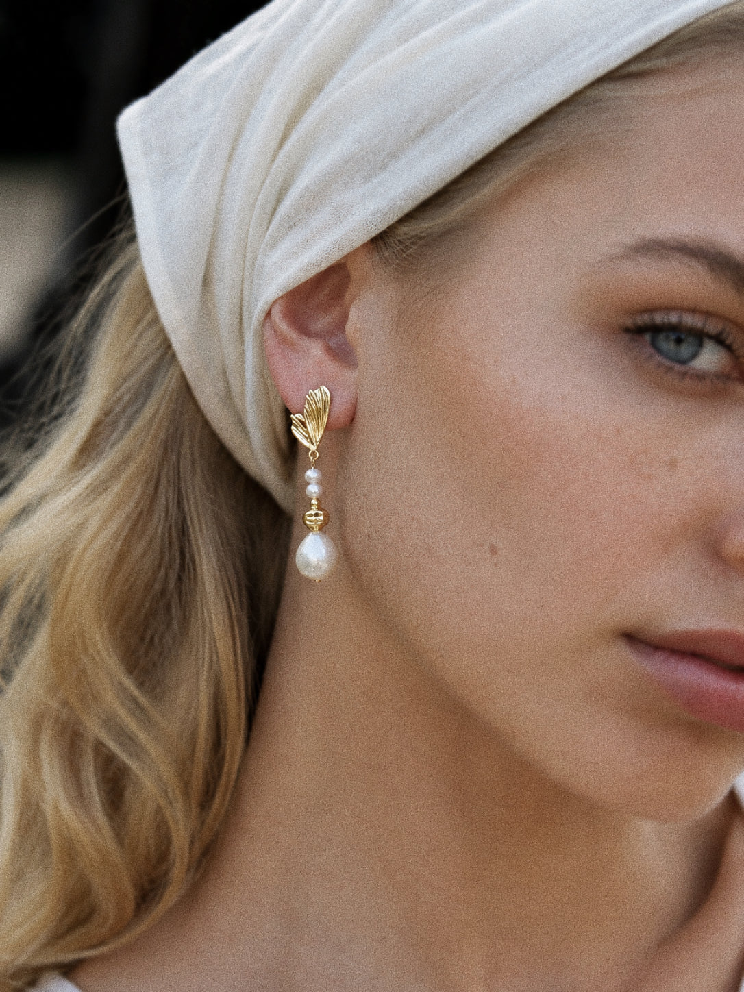 Linden baroque pearl drop earrings worn on the ear, showing their sculpted gold leaves and approximately 5 cm length.
