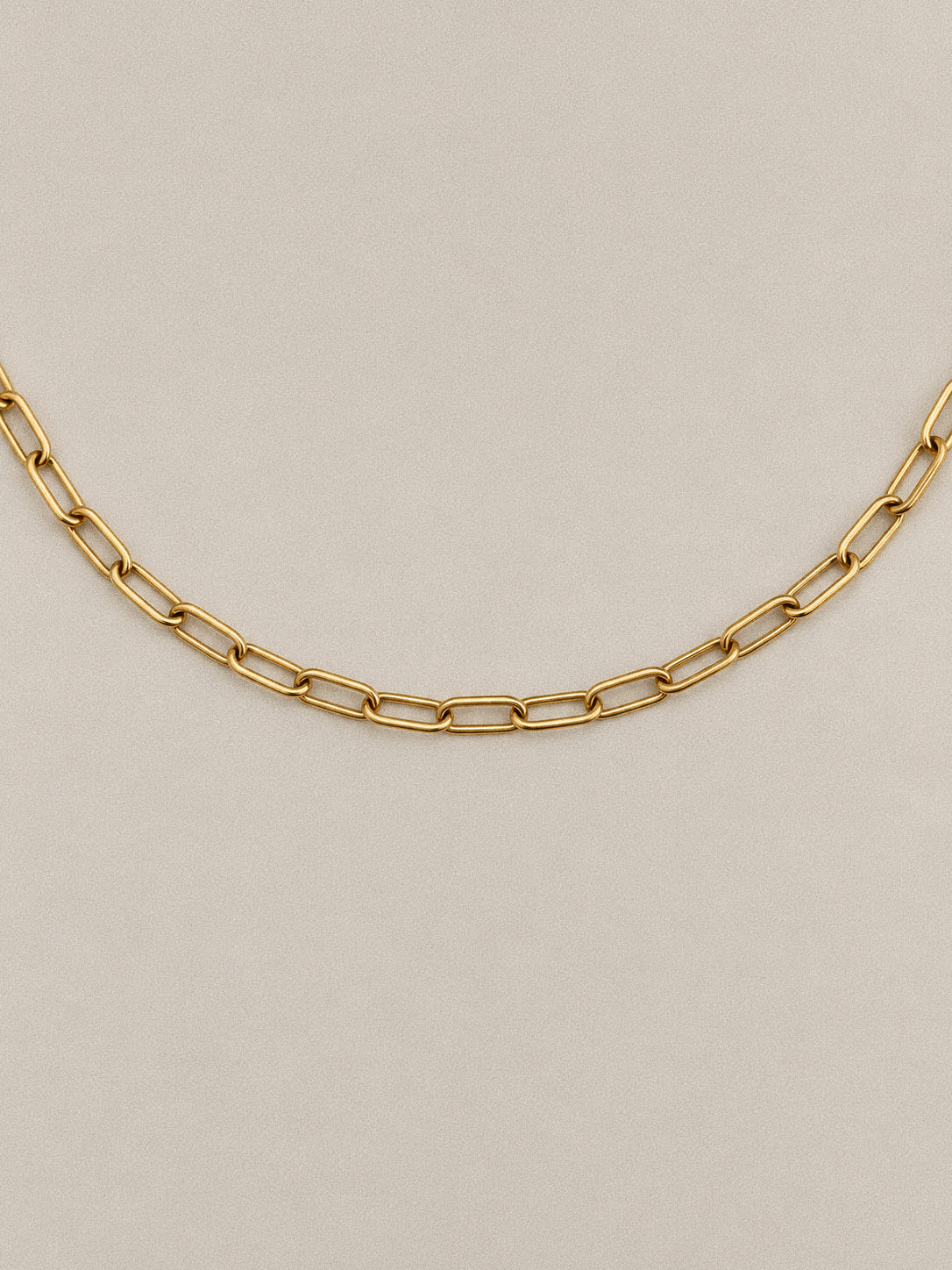Front view of Linea gold-tone paperclip chain necklace, showing elongated links with rounded ends against a taupe background.