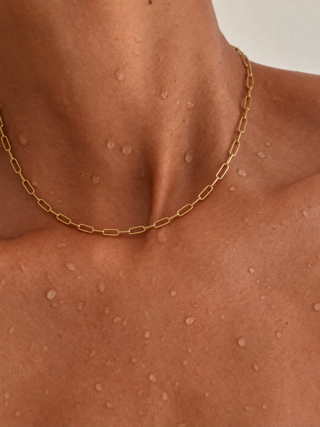 Linea gold-tone paperclip chain necklace worn alone around a model's neckline, with water droplets visible on the skin.