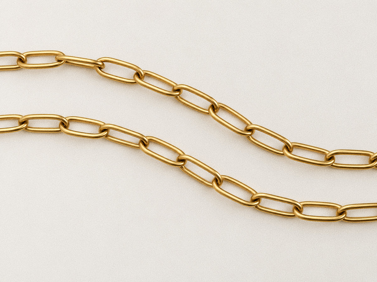Detail of Linea's gold-tone paperclip links, showing their smooth surfaces and rounded rectangular shape on an ivory background.