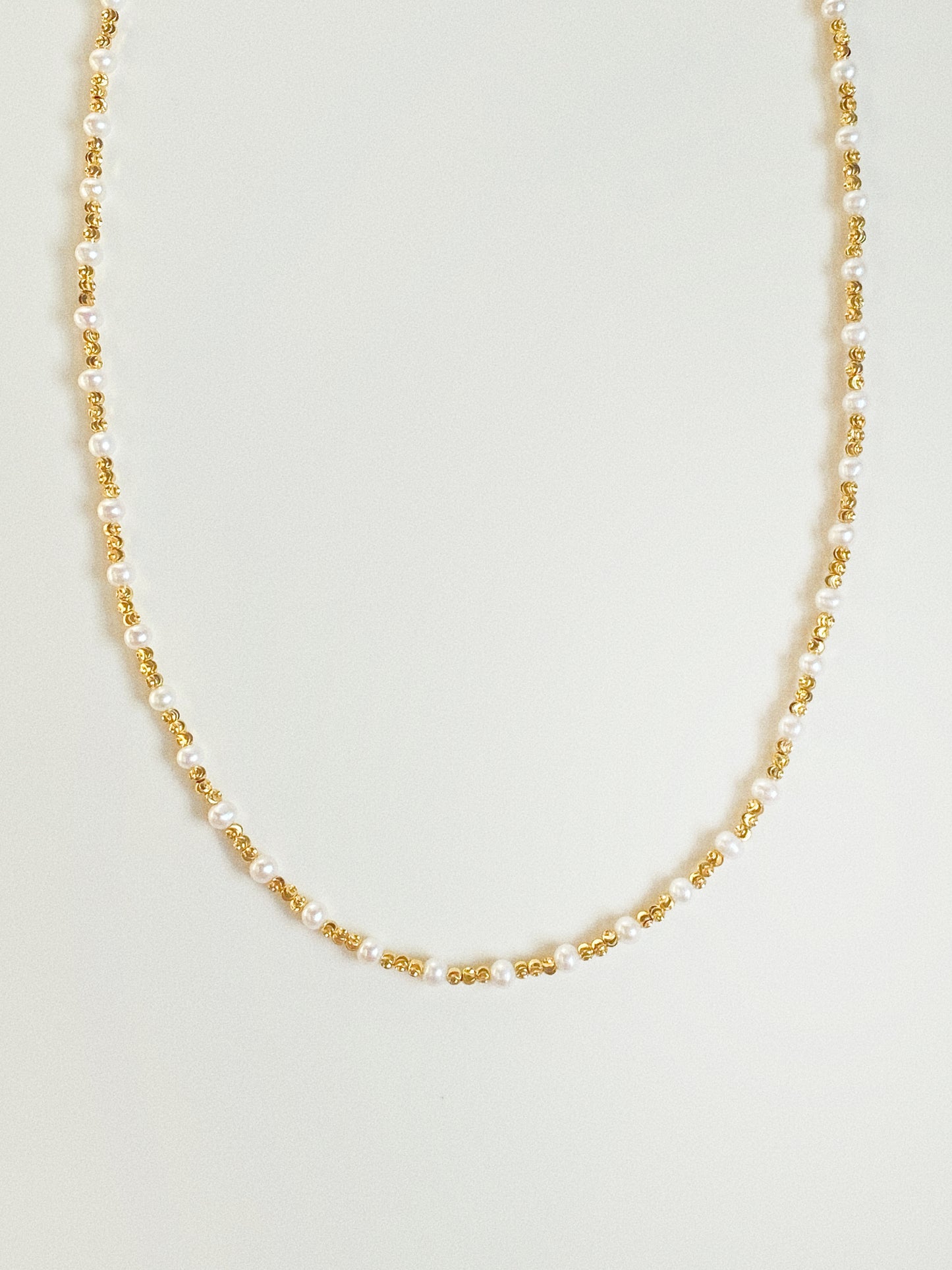 Long pearl and diamond-cut gold bead necklace by Deja Vu Jewellery shown vertically on neutral background