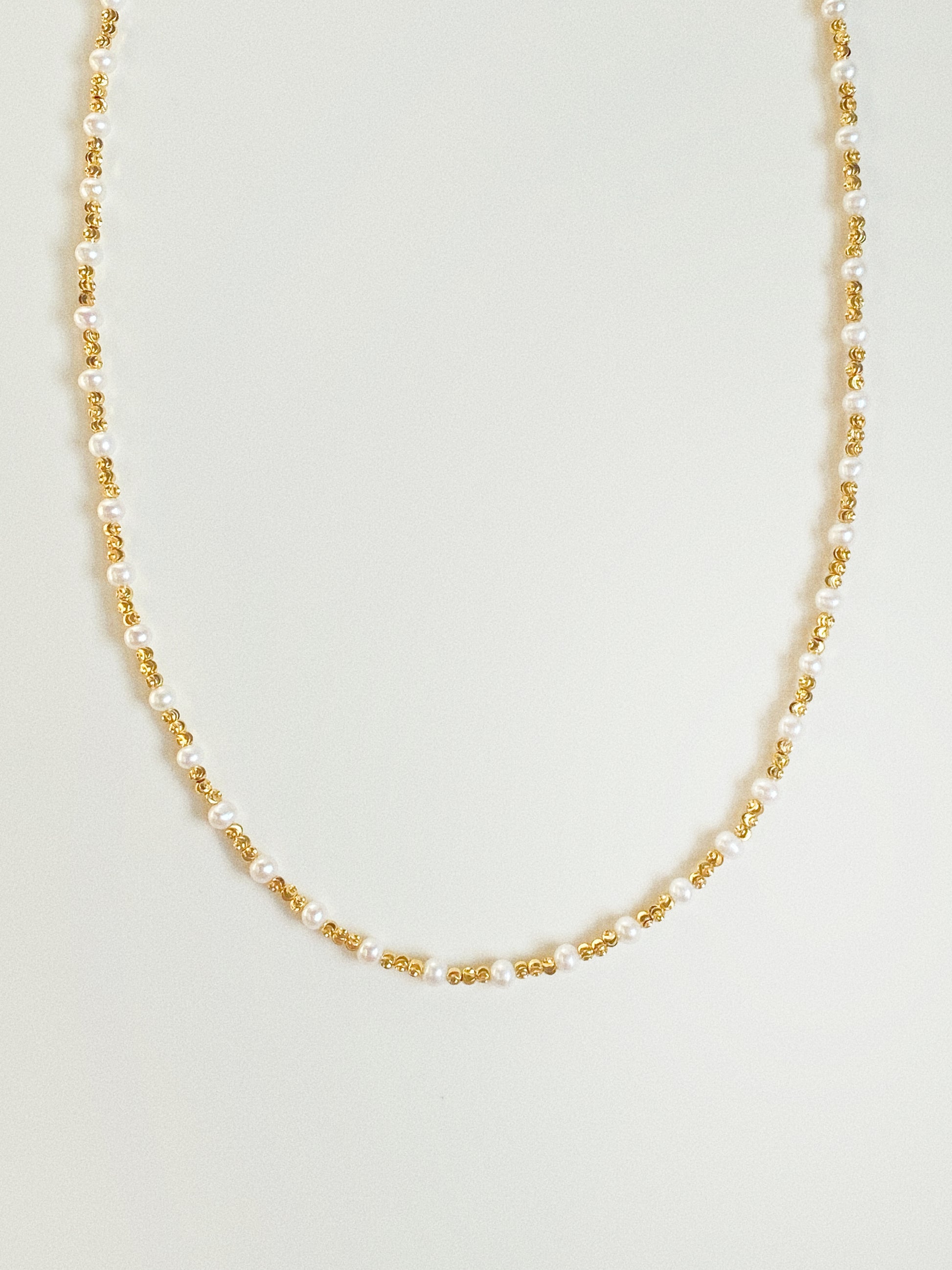 Long pearl and diamond-cut gold bead necklace by Deja Vu Jewellery shown vertically on neutral background