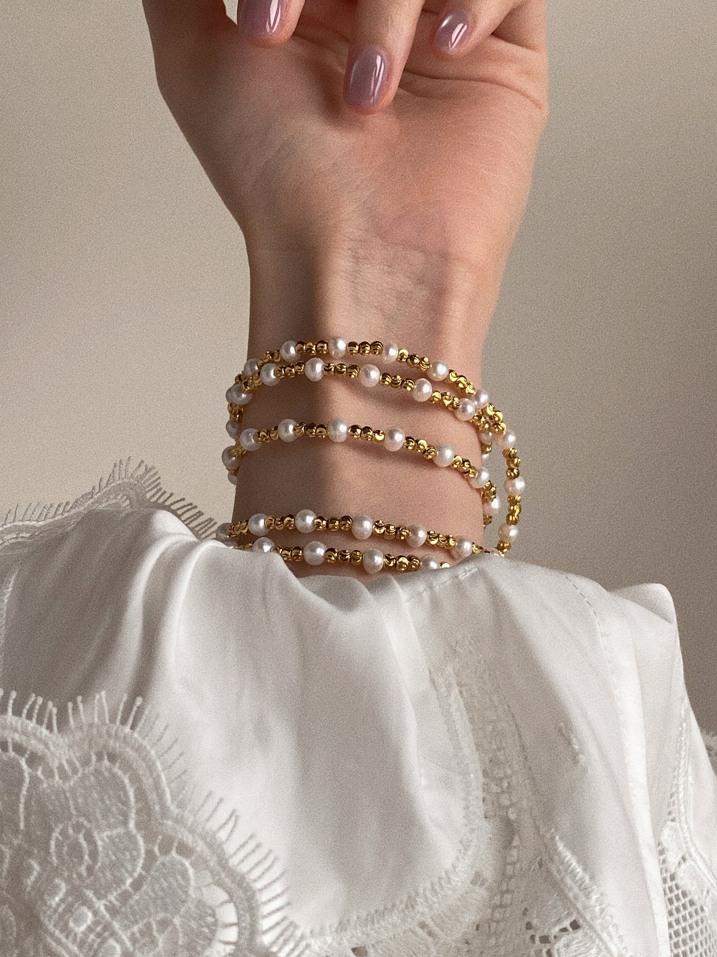 Long pearl and gold bead necklace wrapped multiple times around the wrist as a stacked pearl bracelet