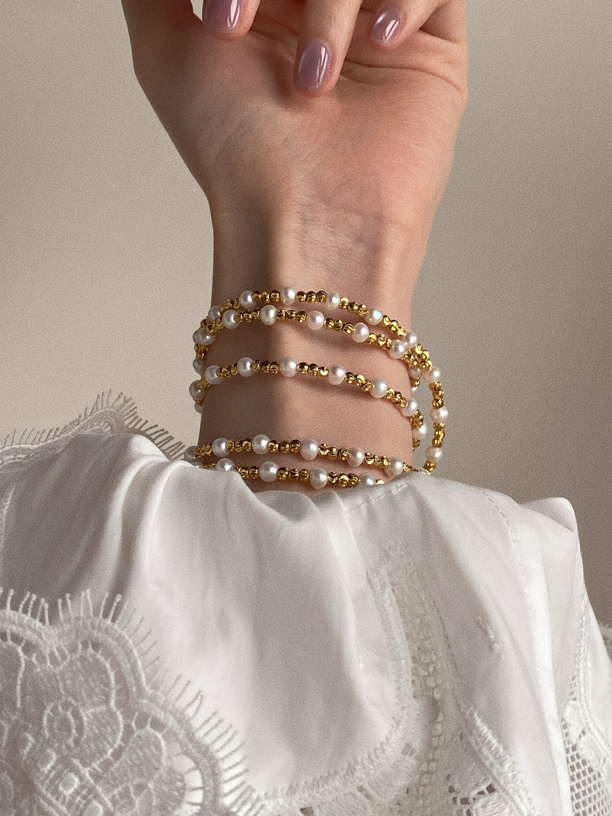 Long pearl and gold bead necklace wrapped multiple times around the wrist as a stacked pearl bracelet