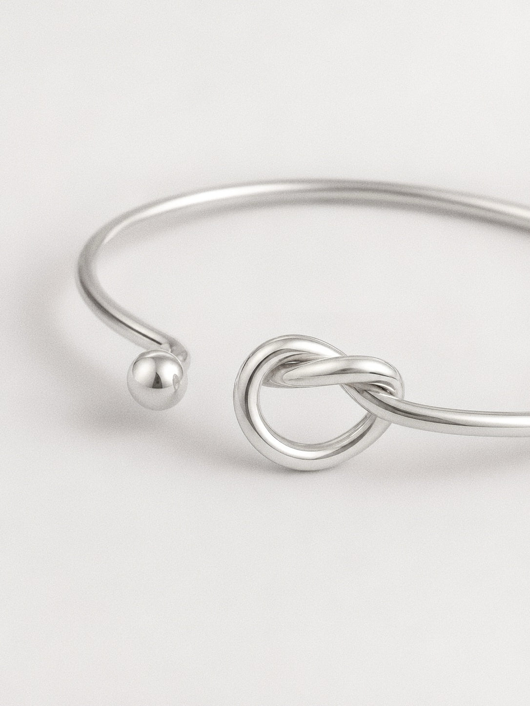 Macro detail of the love knot and rounded silver ball end on a high-shine 925 sterling silver bangle